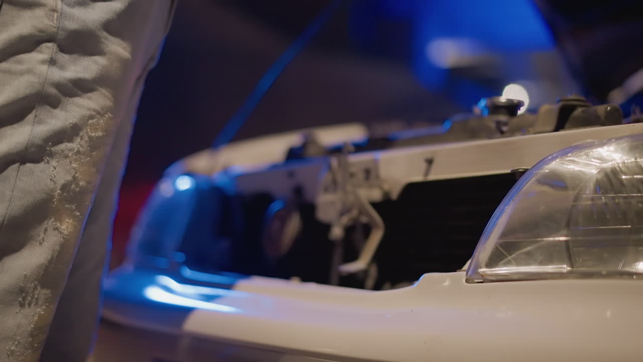 night front grille removal hands adjusting bumper trim closeup of installer prepping aftermarket upgrade under LED streetlights, headlight and mounting clip detail, urban garage vibe with blue