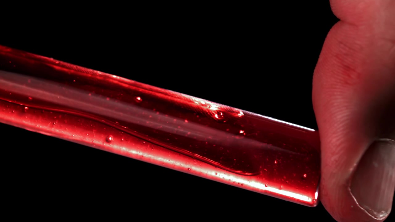 Hand hält Reagenzglas mit roter Flüssigkeit und Blasen