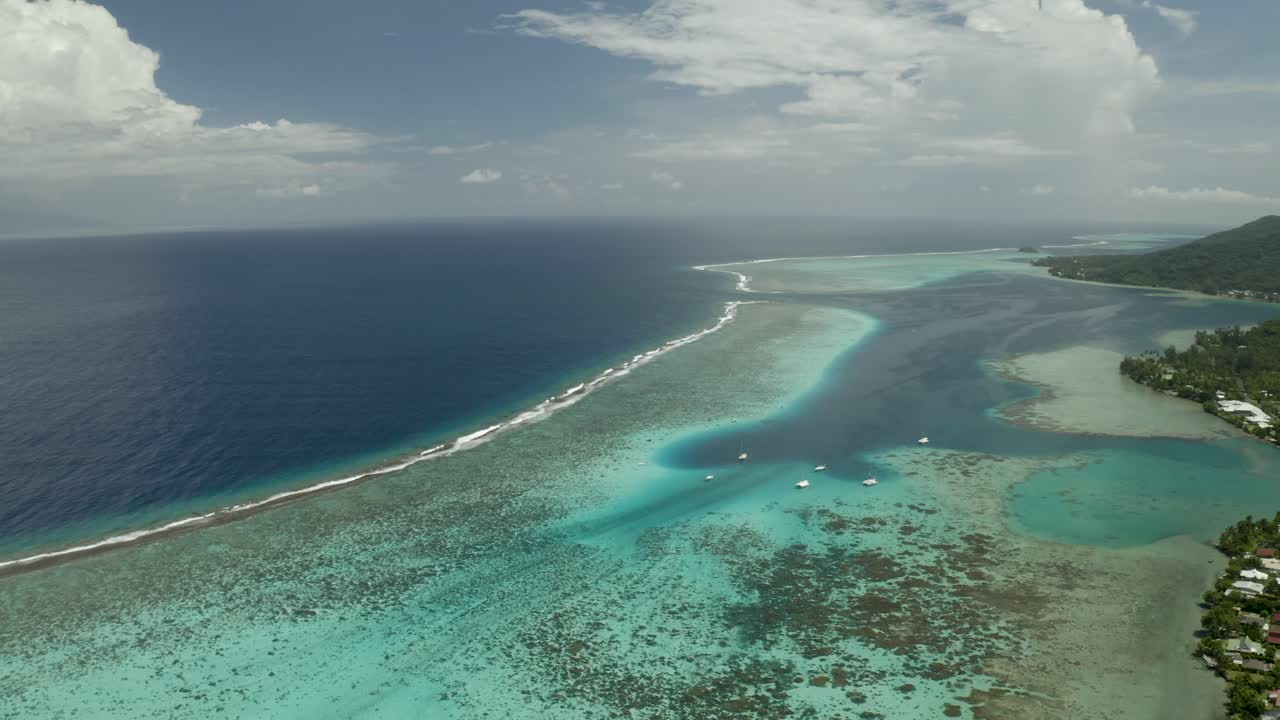 Aerial wide shot flying over the barrier reef encircling Mo'orea island in French Polynesia
