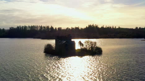 aerial pullback of o'flaherty tower house silhouetted against the calm ballynahinch lake, connemara