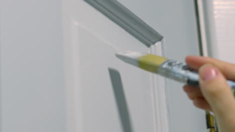 female hand gently using paintbrush to apply white paint onto wooden door doing diy work to decorate home house 4k