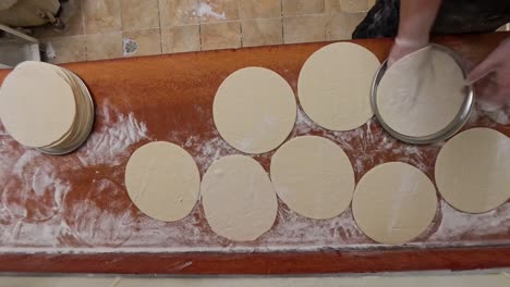 worker puts raw pizza dough pies onto metal plates into a stack.