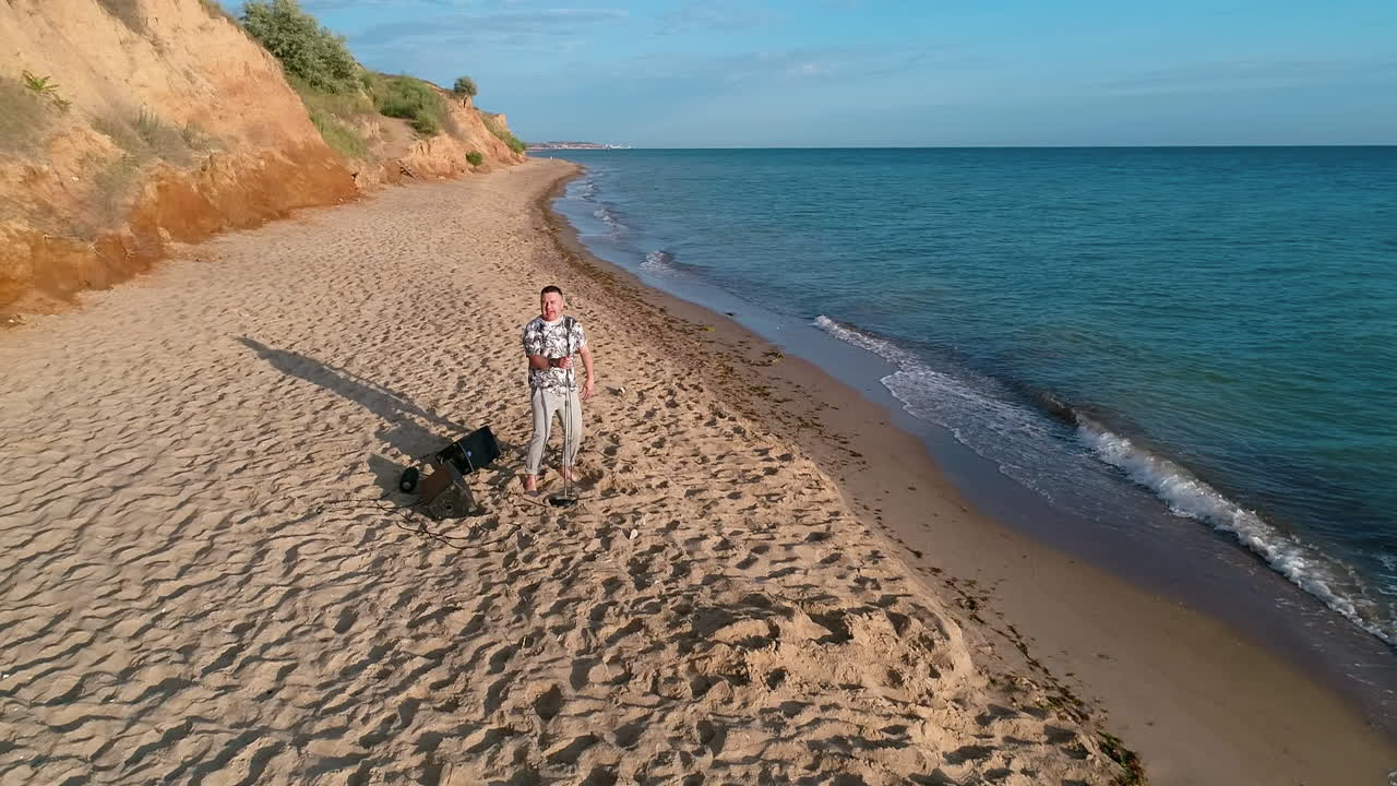 Man singing into microphone on beach. Aerial view of musician sings into the microphone on beach