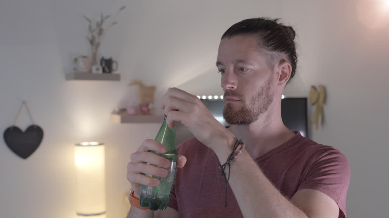 el hombre está abriendo una botella de agua de plástico y bebiendo de ella, entorno doméstico interior, cámara lenta, concepto de conquista de la sed