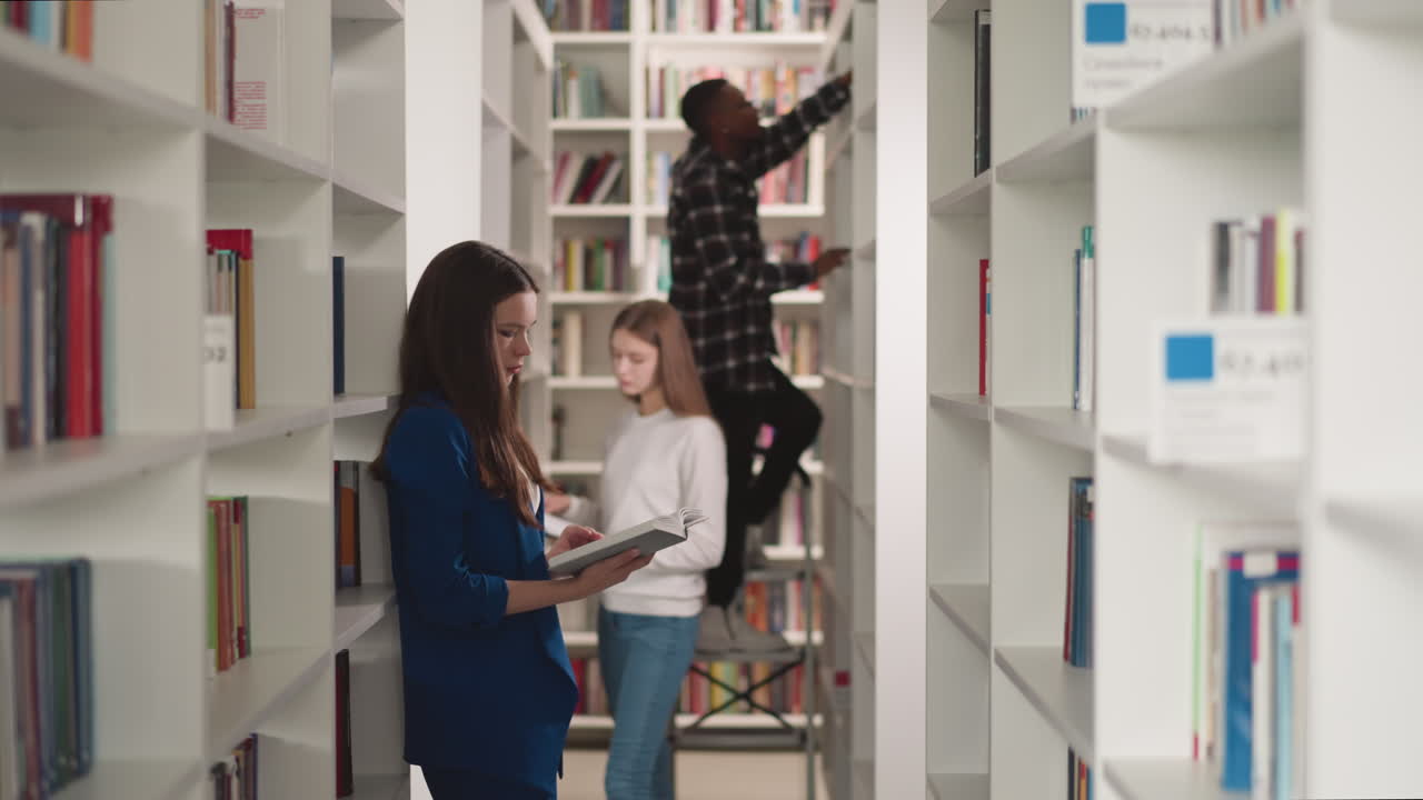 Students work with literature in public library. Young women read books and black man stands on step ladder in bookstore. College education