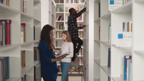 los estudiantes trabajan con literatura en la biblioteca pública. las mujeres jóvenes leen libros y el hombre negro se para en la escalera de la librería. educación universitaria