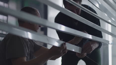 Close-up-Two-male-painters-prepare-steel-metal-elements-for-painting-by-fixing-them-on-suspensions.-painting-plant.-slow-motion-filming.