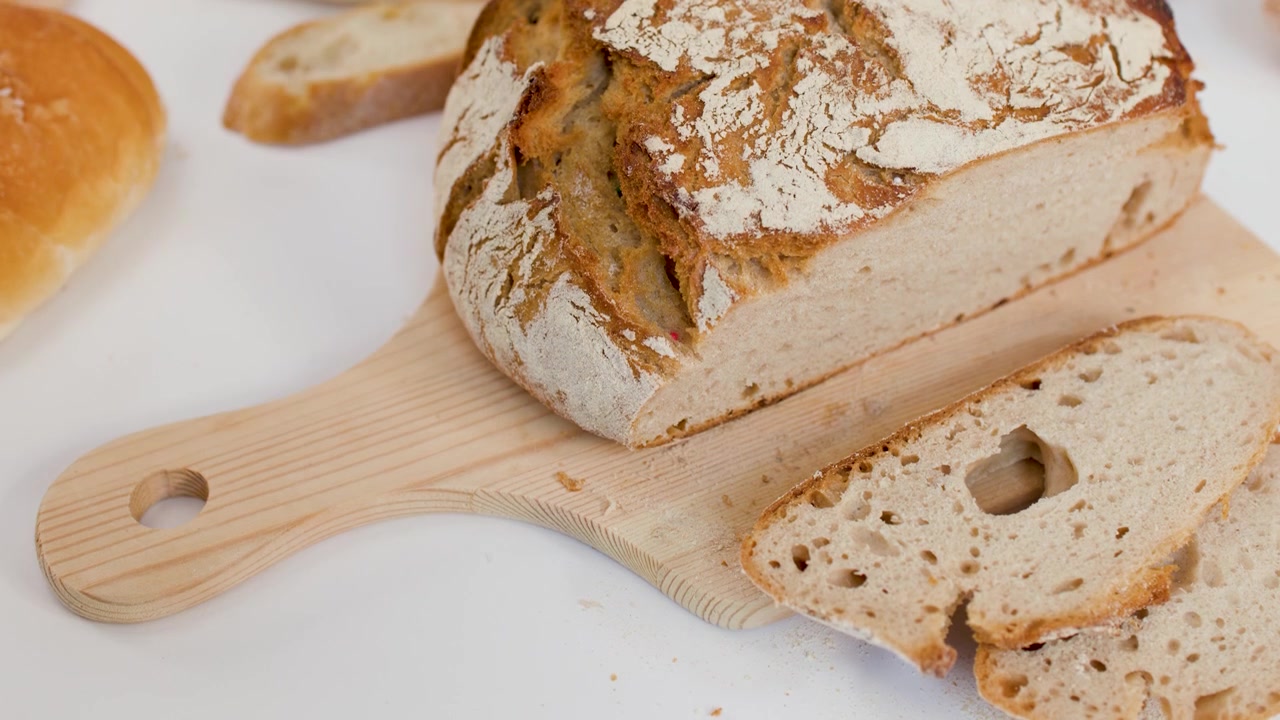 A hand picks up a slice of crusty sourdough bread from a wooden cutting board.