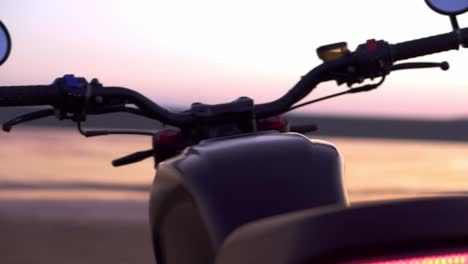 Motorcycle-items-close-up:-bottom-view,-steering-wheel,-mirrors-on-blurred-sunset-under-water-background