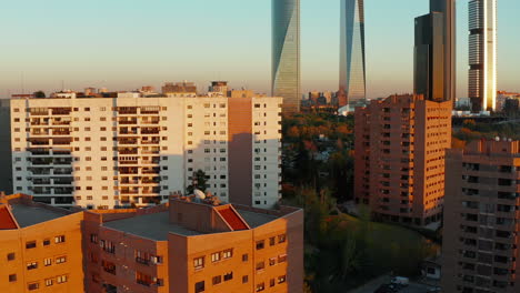 Vorwärts-Fliegen-über-Farbige-Mehrfamilienhäuser-In-Wohnsiedlungen,-Die-Von-Der-Abendsonne-Beleuchtet-Werden.-Moderner-Hochhaus-Büroturm-Im-Hintergrund.