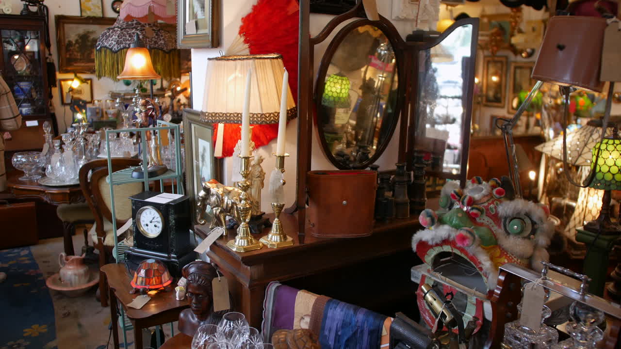 A woman browsing through a cluttered antique shop filled with various vintage items, including brass candlesticks, a decorative clock, and an ornate mirror.