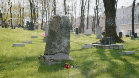 tombstone with a red rose and a grave candle on the grass in a graveyard on a sunny day 1