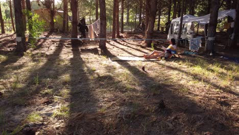 aerial flight inside campsite showing relaxing woman reading book during sunset time in woodland