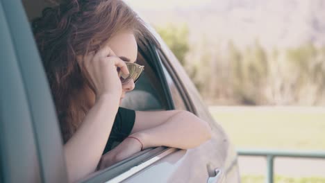 Hübsche-Frau-Lehnt-Sich-Aus-Dem-Autofenster-Und-Setzt-Eine-Sonnenbrille-Auf