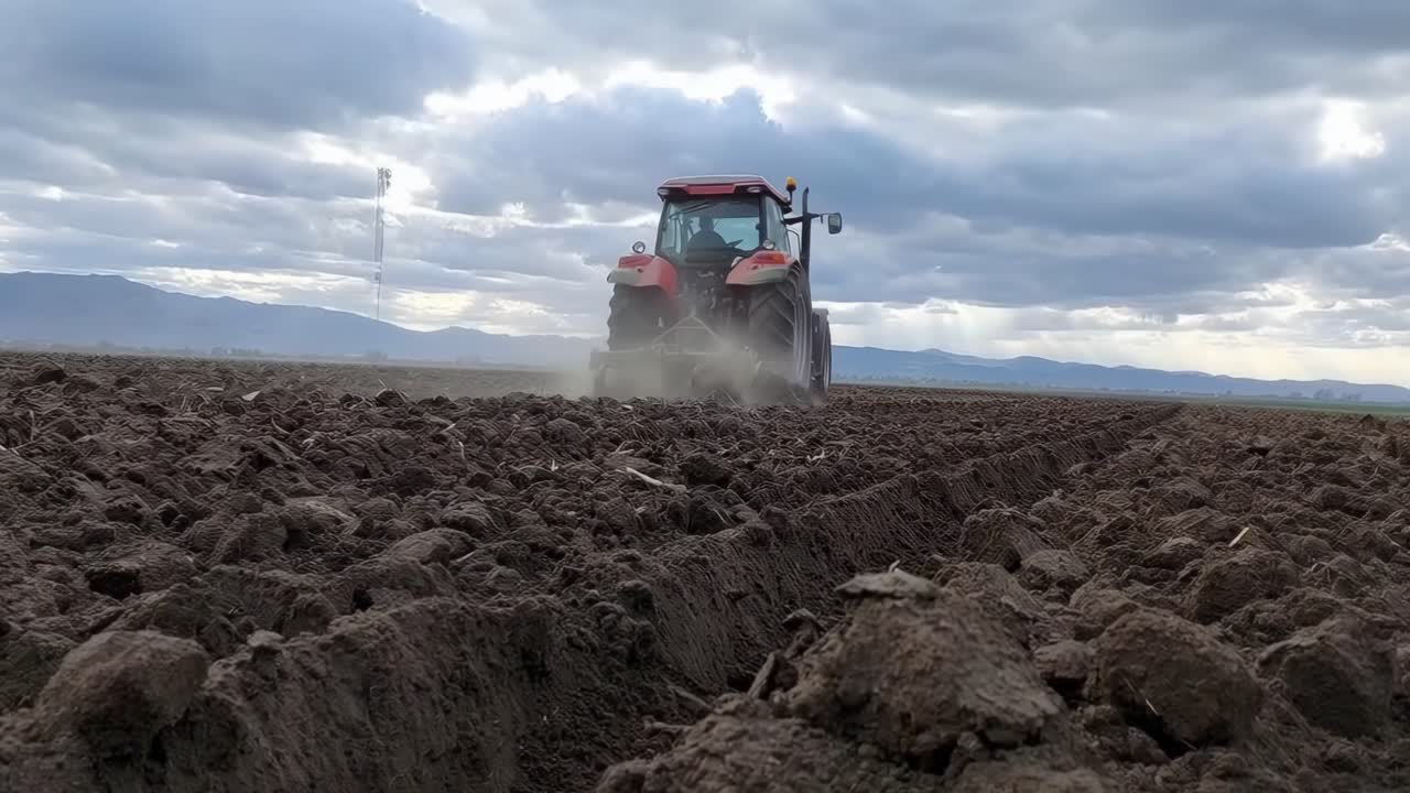 Lavvinkelvideo af en traktor, der pløjer en mark under en skyet himmel, viser landbrugsliv