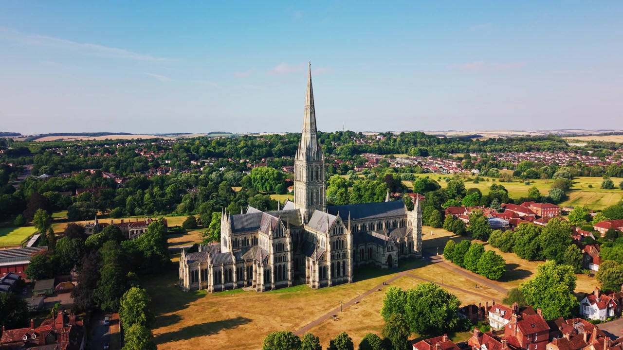 Szeroki widok z drona na Katedrę w Salisbury, jej średniowieczną iglicę, zabytkowe tereny i otaczający zielony krajobraz miejski w pogodny letni dzień w Wiltshire