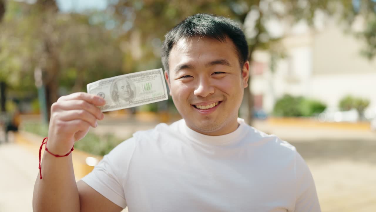 젊은 중국인 남자가 공원에서 자신감 있게 웃으며 달러를 깨뜨린다.