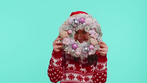 una chica adulta sonriente con un suéter de navidad rojo sostiene el dedo del punto de elevación en el juguete de la corona festiva