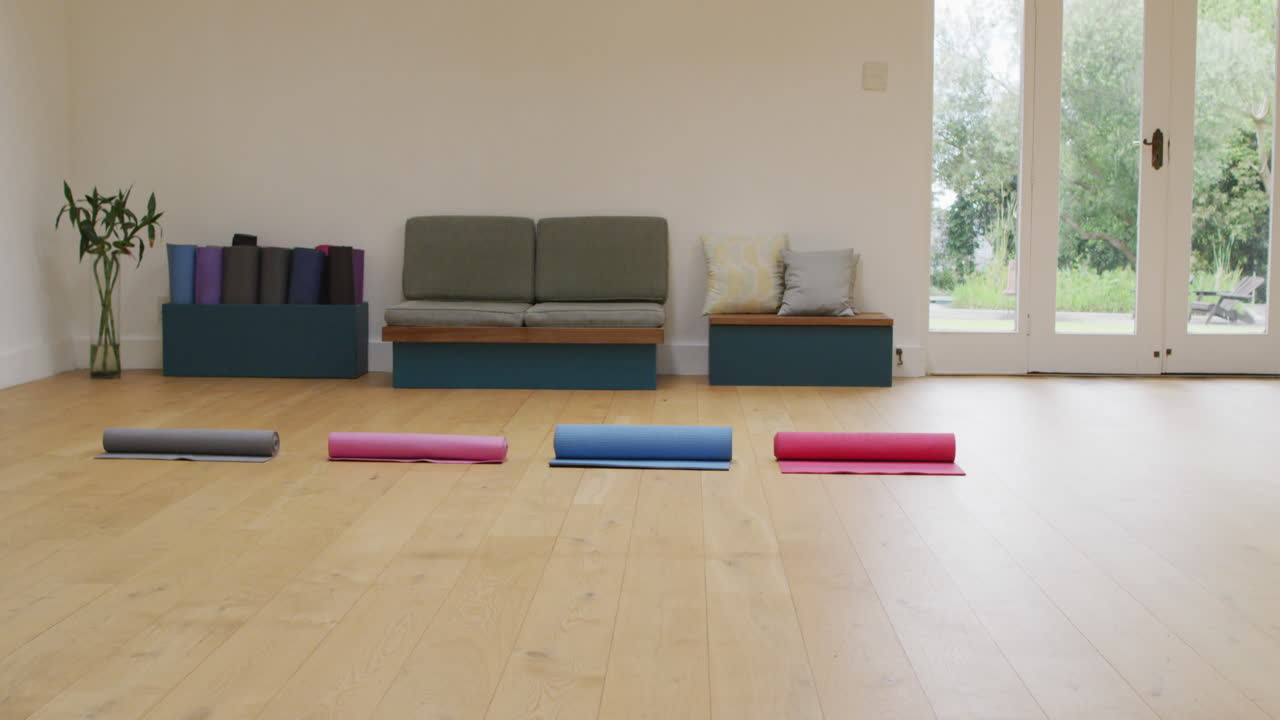 나무 바닥 과 정원 으로 가는 문 을 가진  빈 스튜디오 에서 네 개 의 요가 매트 를 굴러 올렸다
