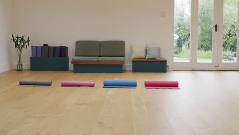 four rolled up yoga mats in empty studio with wooden floor and doors to garden