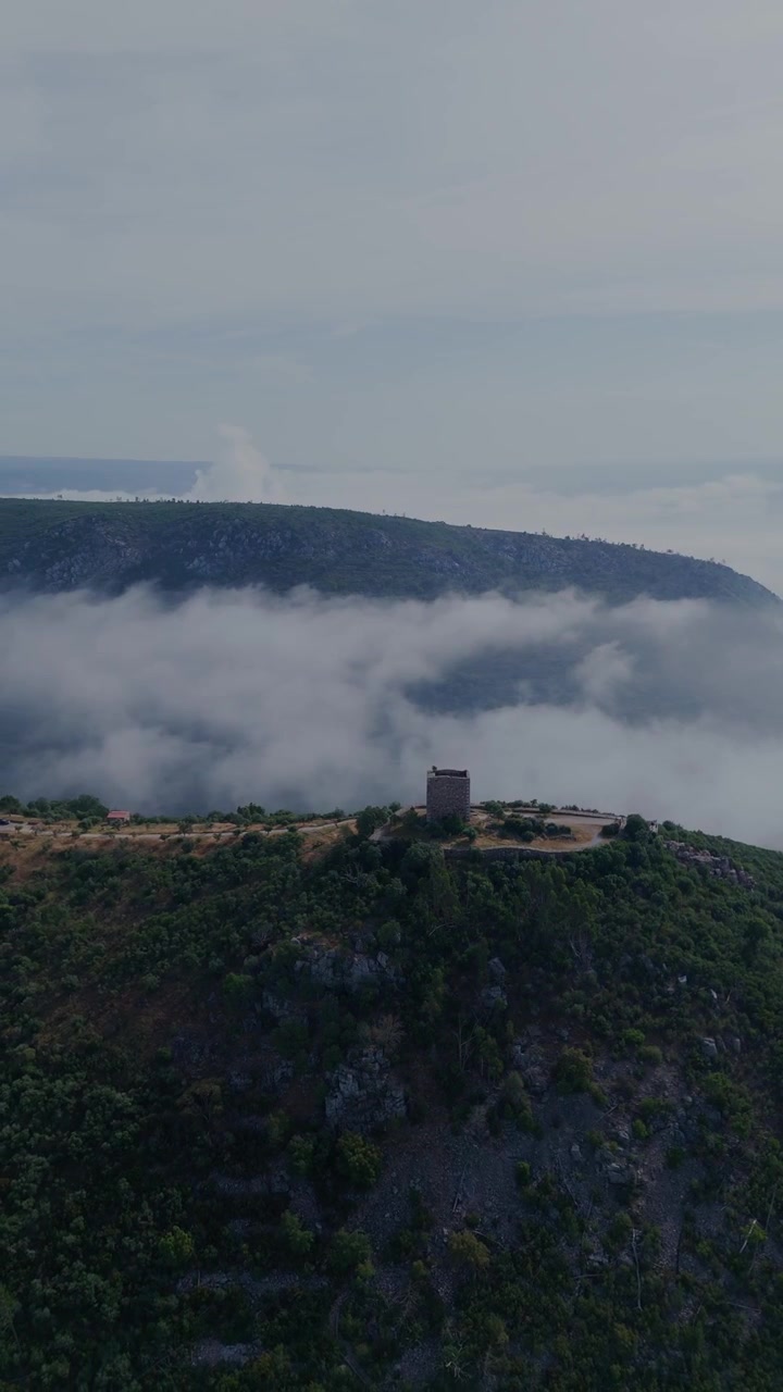 Vertikal drönarorbit som drar sig tillbaka från Castelo de Rodao och avslöjar kapellet, floden Tejo, det omgivande landskapet och morgondimman.