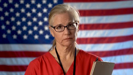 portrait of nurse set against an out of focus us flag showing disappointment and sadness