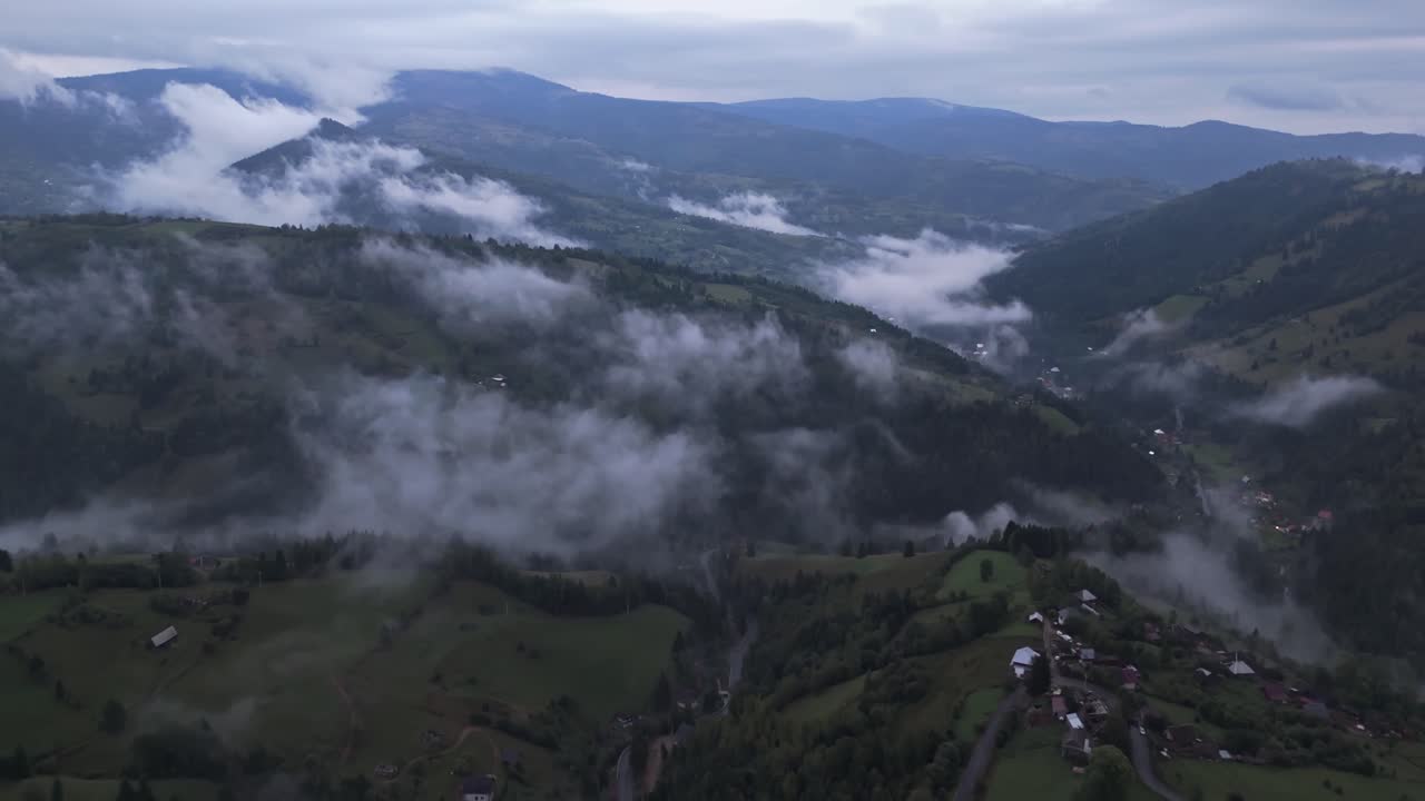 Aerial drone view of Mătișești village in the Apuseni Mountains of Romania, with layers of fog drifting between forested hills and valleys, creating a peaceful and moody mountain landscape