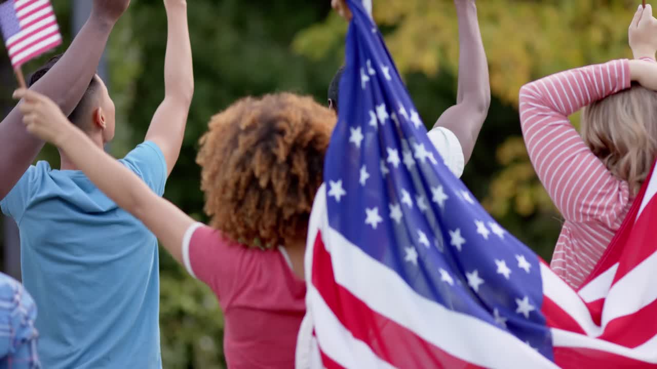 Happy diverse group of friends holding flags of usa and celebarting in garden, slow motion