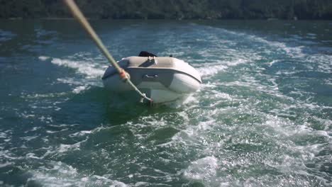 Inflatable-boat-being-towed-on-rope-behind-boat-on-sea-of-New-Zealand