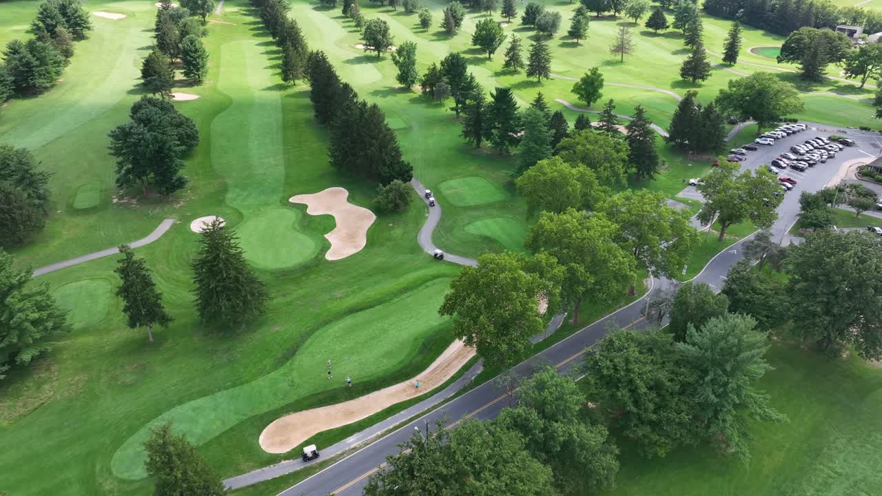 Aerial tracking shot of car arriving golf club golf course during sunny day in America. Green lawn of golf course in noble club