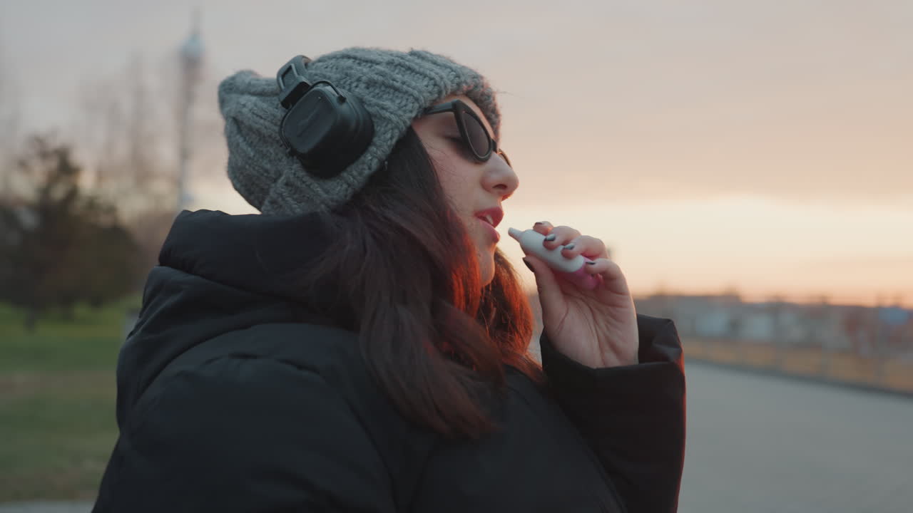 Signora con cuffie che si gode il tramonto serale. Persona seduta pacificamente e ascoltando musica al crepuscolo. Individuo seduto su una panchina che vive momenti tranquilli al tramonto mentre è immerso nella musica.