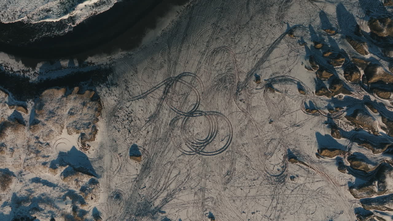 Drone aerial top-down view of circular and overlapping vehicle tire tracks on a snow-covered coastal plain in Iceland during winter. Off-road driving and Nordic wilderness concept