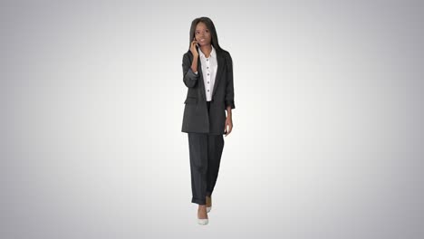 casual african american businesswoman talking on phone while walking on gradient background