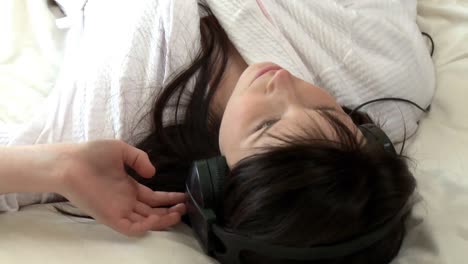 charming woman listening music lying on bed