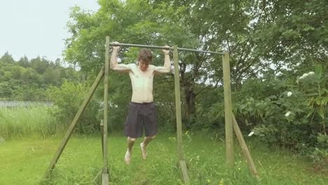 young fit man doing behind-neck pullups outdoors in nature slow-motion