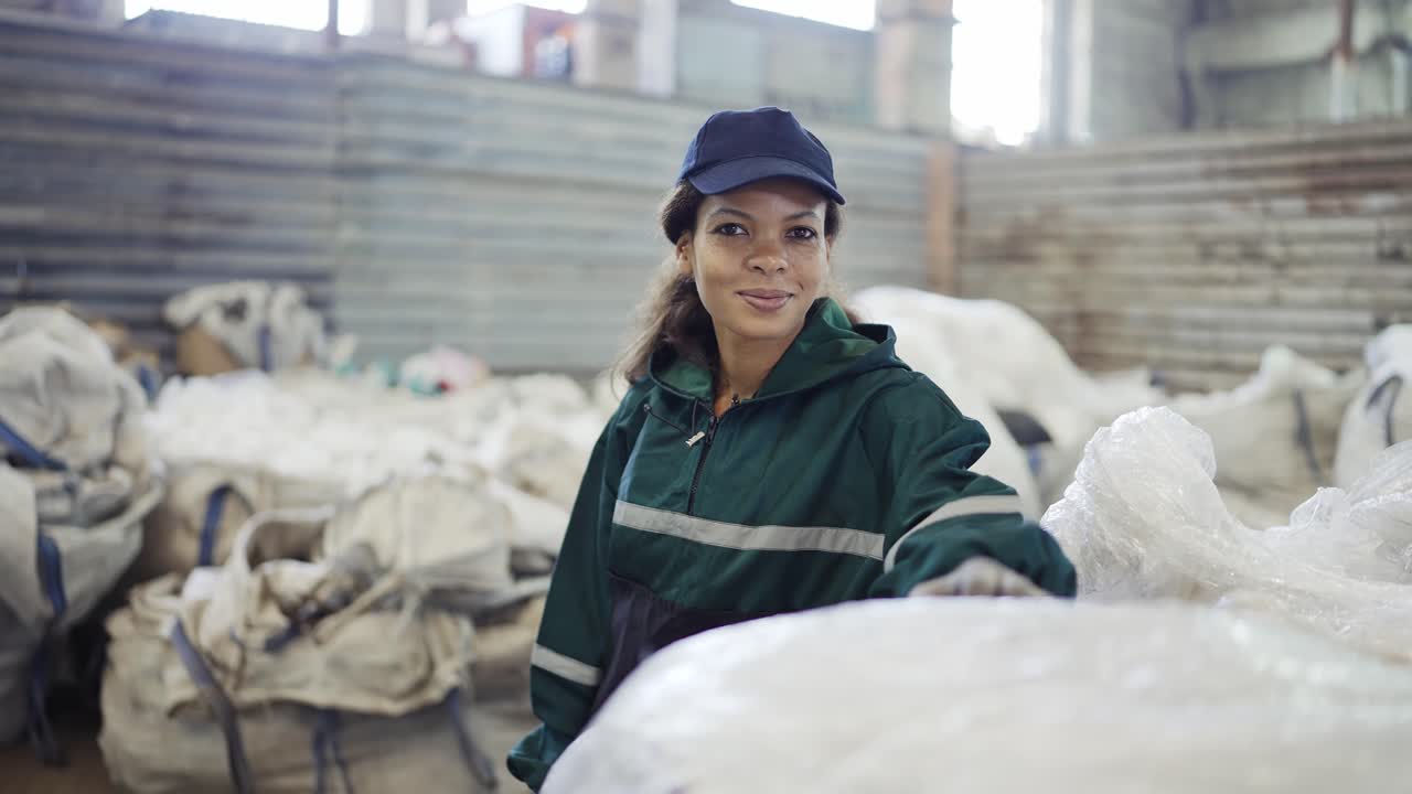 y una mujer afroamericana con un uniforme especial clasifica polietileno en una planta de reciclaje de residuos.