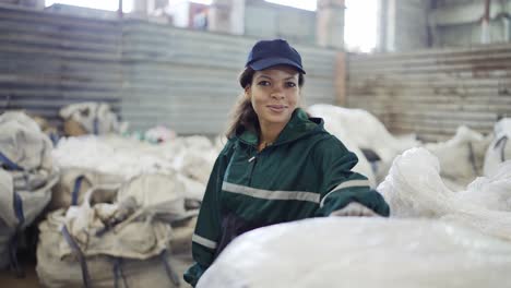 and african-american woman in a special uniform sorts polyethylene at a waste recycling plant. processing of raw materials