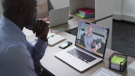 hombre mayor afroamericano teniendo una videollamada con un colega masculino en una computadora portátil en la oficina