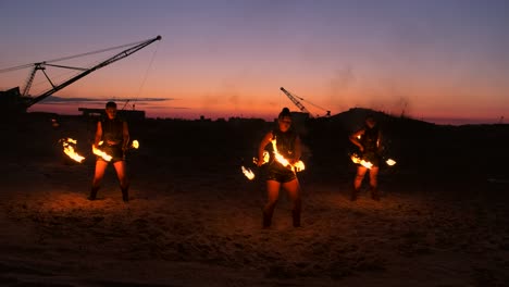 professional artists show a fire show at a summer festival on the sand in slow motion. fourth person acrobats from circus work with fire at night on the beach.