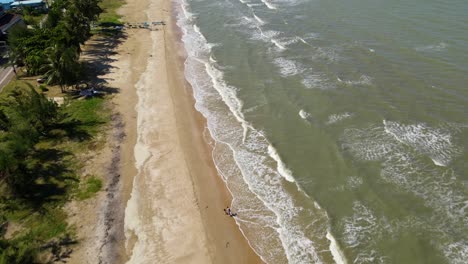 Una-Filmación-Aérea-Que-Muestra-Una-Playa,-Olas-Que-Forman-Aguas-Bravas,-Dos-Personas-Caminando-En-La-Playa