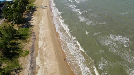 una filmación aérea que muestra una playa, olas que forman aguas bravas, dos personas caminando en la playa