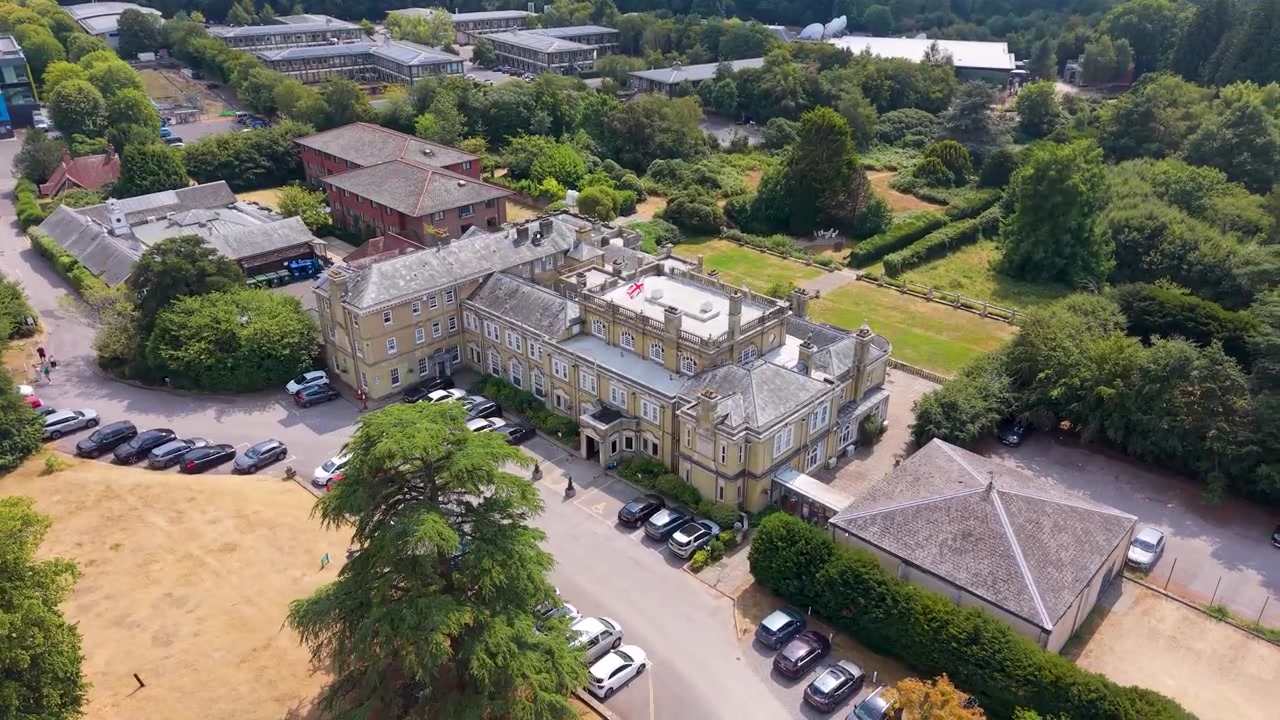 Drone kredser fra siden til fronten af Chilworth Manor nær Southampton, Hampshire, og viser parkeringspladsen, græsplænerne og herregårdens bygninger.