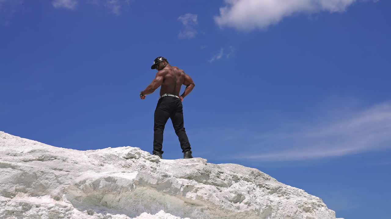 Strong athletic man fitness model. Low angle view of the guy with naked torso showing six pack abs. Clear blue sky on the background