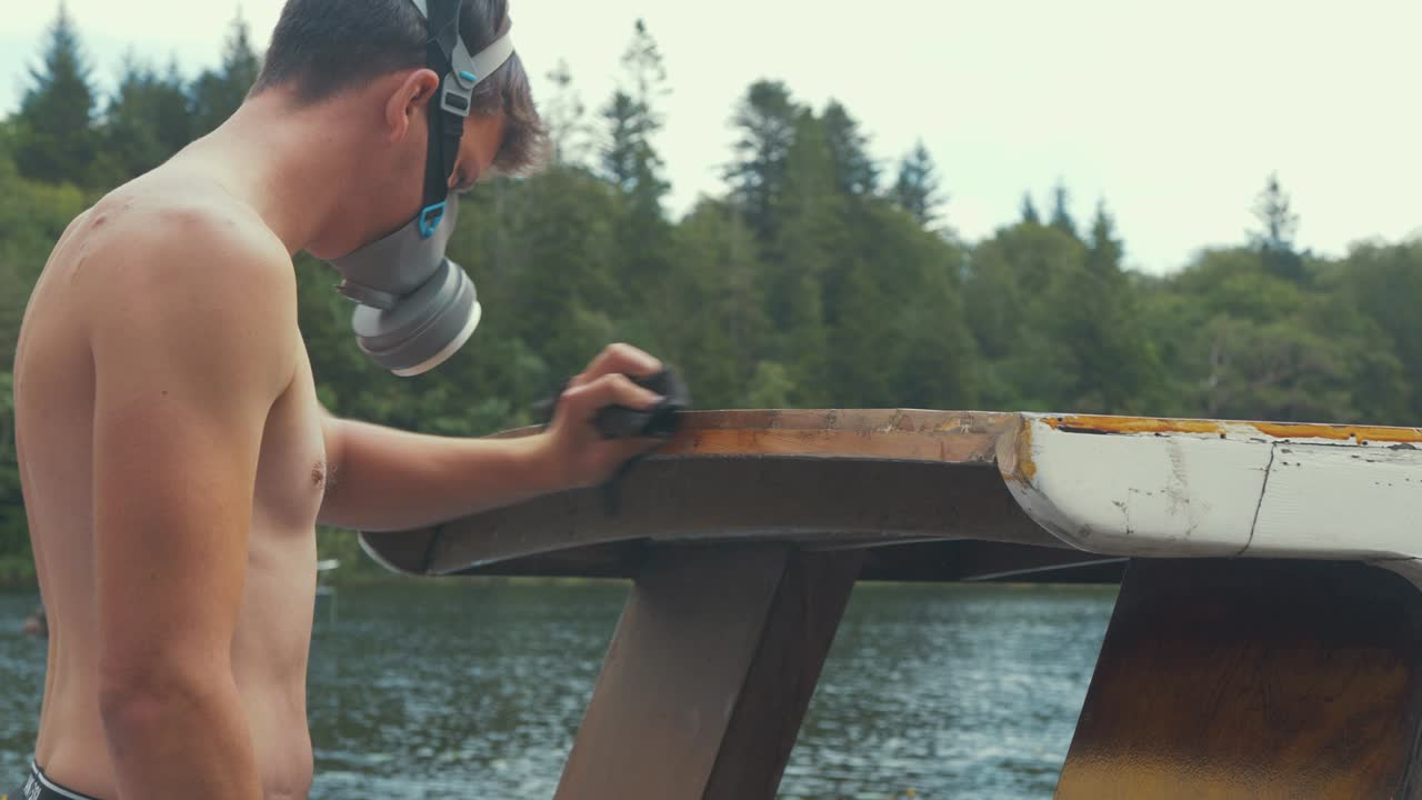 손 샌딩 후 오두막 지붕 가장자리를 닦는 젊은 토플리스 목수