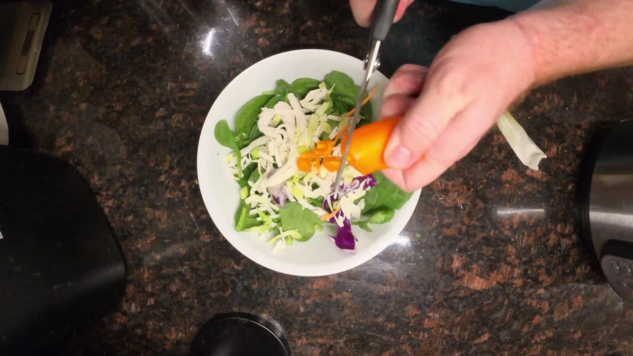 Top view showing close up of chef's hands cutting orange bell pepper over a fresh salad