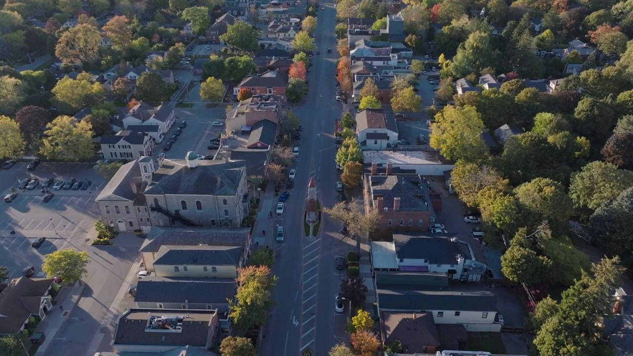 Una vista aerea lungo Queen Street a Niagara-on-the-Lake, la Torre dell'Orologio Commemorativa che si erge tra edifici storici alberati con la costa oltre, in una limpida giornata autunnale.