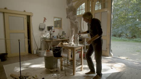 sculptor placing plaster on sculpture in workshop - wide