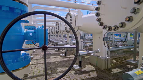 long row of large blue manual valves on a natural gas pipeline at an industrial pumping and transport station, vital infrastructure for the energy industry in latvia - panning reveal