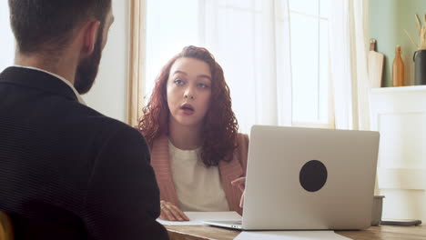 young businesswoman debating and consulting paper report with her male colleague sitting at table in the office