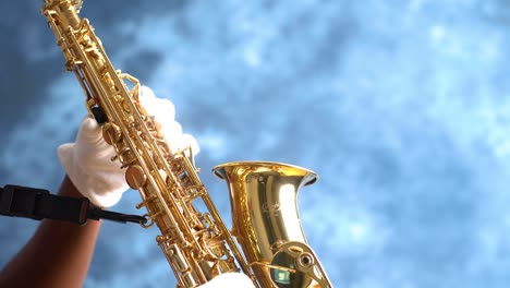 mano masculina adulta africana con guantes blancos tocando un saxofón alto atado con un fondo azul